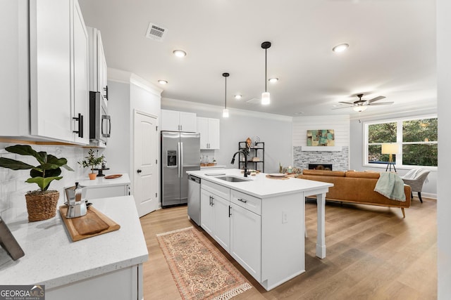 kitchen featuring hanging light fixtures, stainless steel appliances, a center island with sink, sink, and white cabinetry