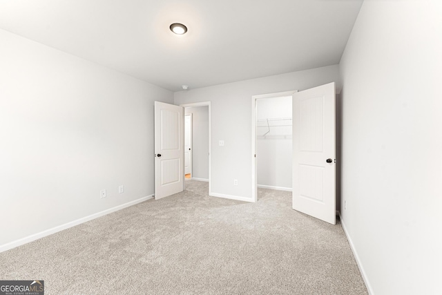 unfurnished bedroom with a walk in closet, light colored carpet, and a closet