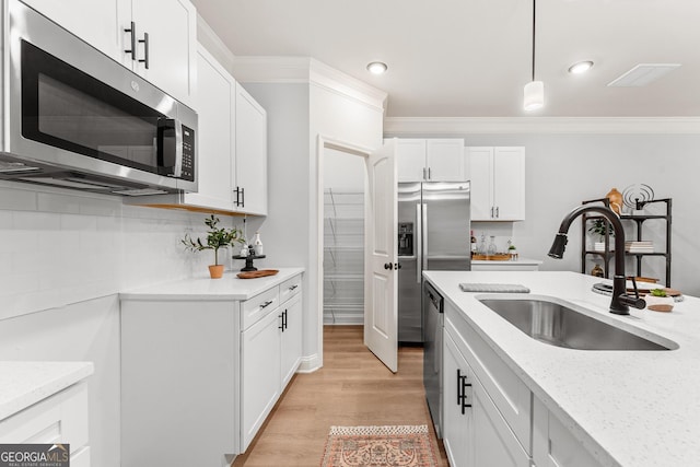 kitchen featuring hanging light fixtures, stainless steel appliances, sink, white cabinetry, and light hardwood / wood-style floors