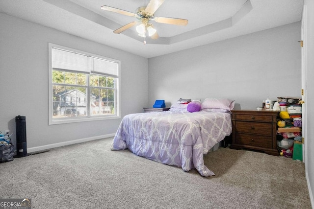 carpeted bedroom featuring ceiling fan and a tray ceiling