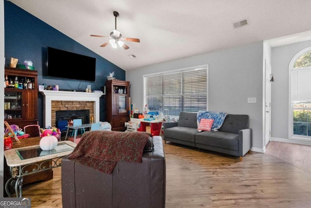 living room with light hardwood / wood-style floors, lofted ceiling, a stone fireplace, and plenty of natural light