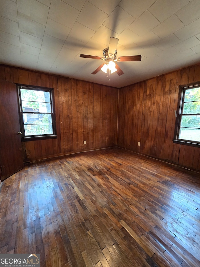 unfurnished room featuring wood walls, dark wood-type flooring, ceiling fan, and plenty of natural light