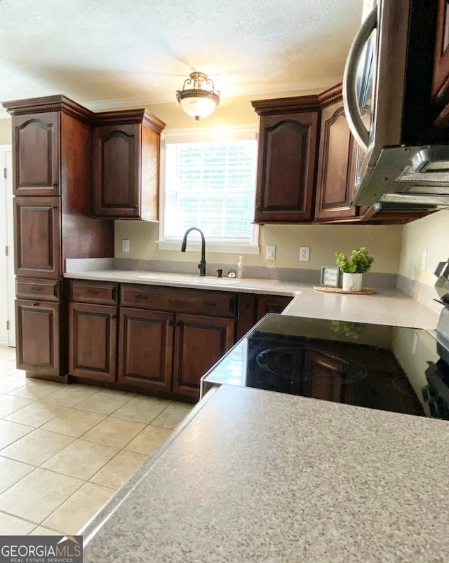 kitchen featuring dark brown cabinets, light tile patterned floors, a textured ceiling, black range oven, and sink