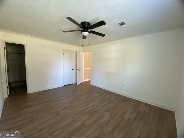 unfurnished bedroom with ornamental molding, a walk in closet, dark hardwood / wood-style floors, and ceiling fan