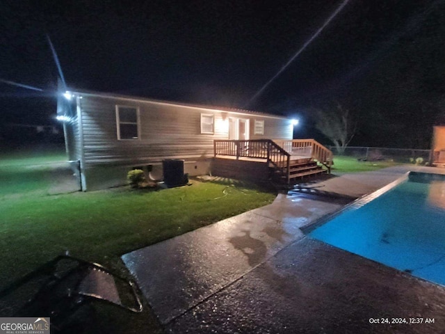 back house at twilight featuring a yard, a pool side deck, and central AC unit