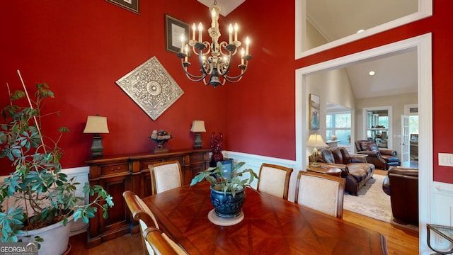 dining room with a chandelier, a wainscoted wall, vaulted ceiling, and wood finished floors