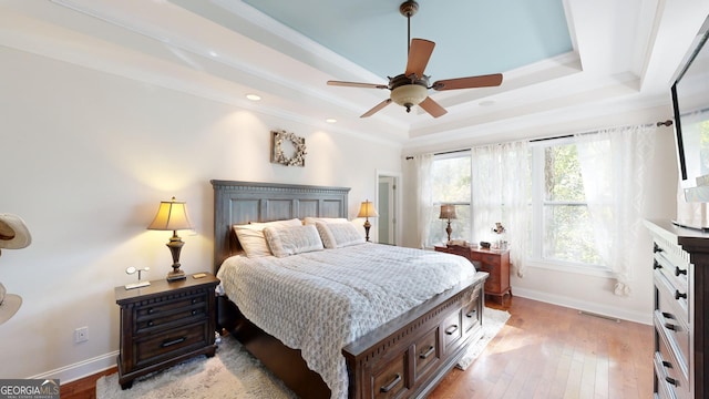 bedroom with light wood-style flooring, crown molding, a tray ceiling, and baseboards