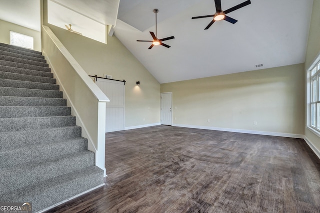 unfurnished living room with dark hardwood / wood-style floors, ceiling fan, high vaulted ceiling, and a barn door