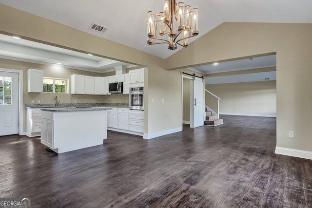 kitchen with appliances with stainless steel finishes, a barn door, hanging light fixtures, white cabinets, and dark wood-type flooring