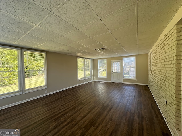 unfurnished room featuring a paneled ceiling, brick wall, and dark hardwood / wood-style flooring