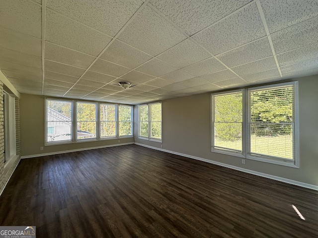 unfurnished living room with baseboards, a paneled ceiling, and dark wood-type flooring