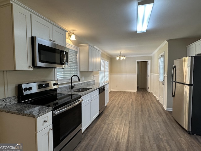 kitchen with appliances with stainless steel finishes, dark wood finished floors, a sink, a notable chandelier, and ornamental molding
