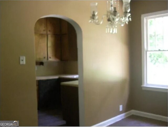 unfurnished dining area with an inviting chandelier, arched walkways, and baseboards