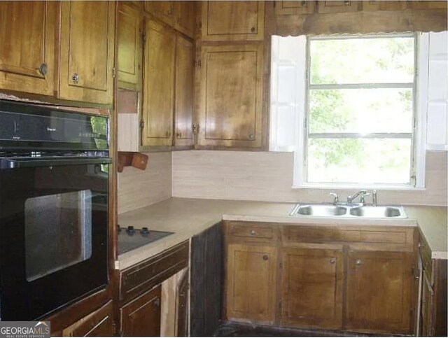 kitchen featuring brown cabinetry, tasteful backsplash, a sink, light countertops, and black appliances