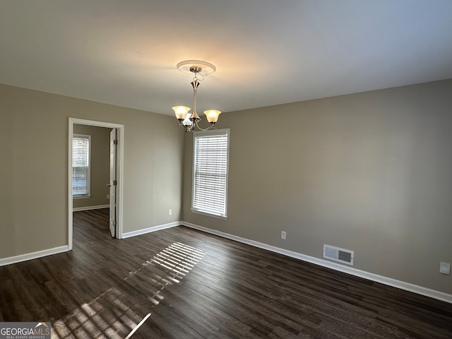 spare room with a chandelier and dark hardwood / wood-style floors