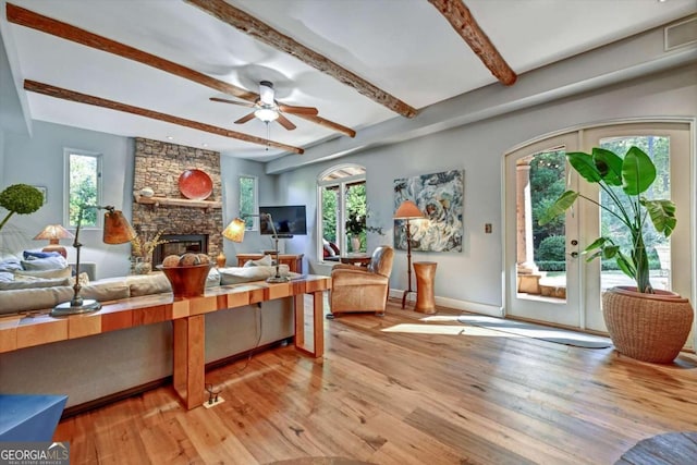 living room featuring light hardwood / wood-style floors, ceiling fan, a stone fireplace, and a wealth of natural light