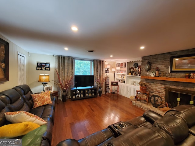 living room with a brick fireplace, built in shelves, and wood-type flooring