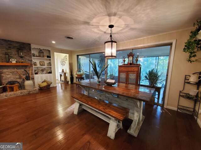 dining room featuring visible vents, built in features, dark wood-style floors, ornamental molding, and a brick fireplace