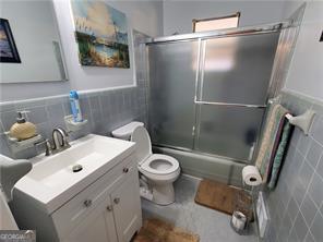 bathroom featuring enclosed tub / shower combo, toilet, vanity, tile walls, and wainscoting