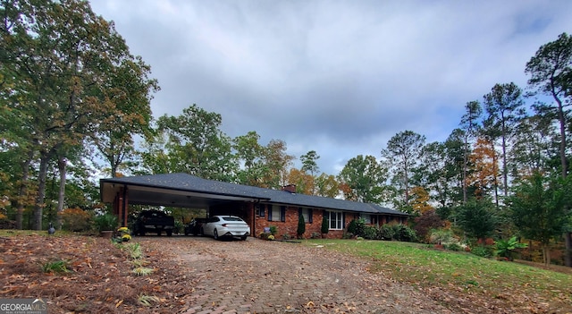 ranch-style house with driveway, brick siding, a chimney, a carport, and a front yard