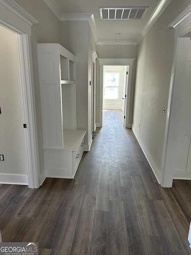 hall with dark wood finished floors, crown molding, baseboards, and visible vents