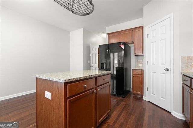 kitchen with dark hardwood / wood-style flooring, a center island, light stone counters, and black fridge