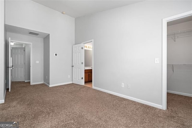 unfurnished bedroom with connected bathroom, a walk in closet, a closet, and light colored carpet