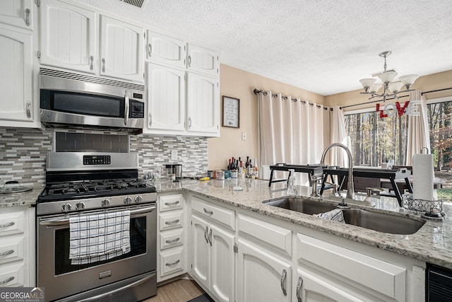 kitchen with decorative backsplash, appliances with stainless steel finishes, sink, white cabinets, and a chandelier