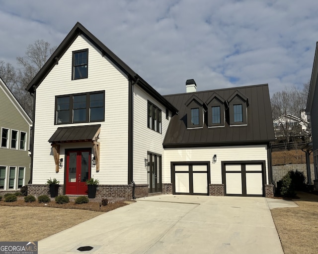 modern inspired farmhouse featuring a standing seam roof, driveway, a chimney, and an attached garage