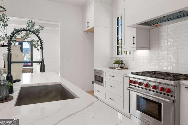 kitchen with designer range, tasteful backsplash, white cabinets, light stone countertops, and premium range hood