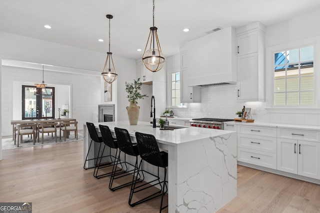 kitchen featuring visible vents, range, light wood-style flooring, custom range hood, and backsplash