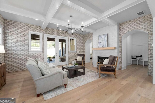 living area featuring light wood-style floors, arched walkways, a brick fireplace, and visible vents