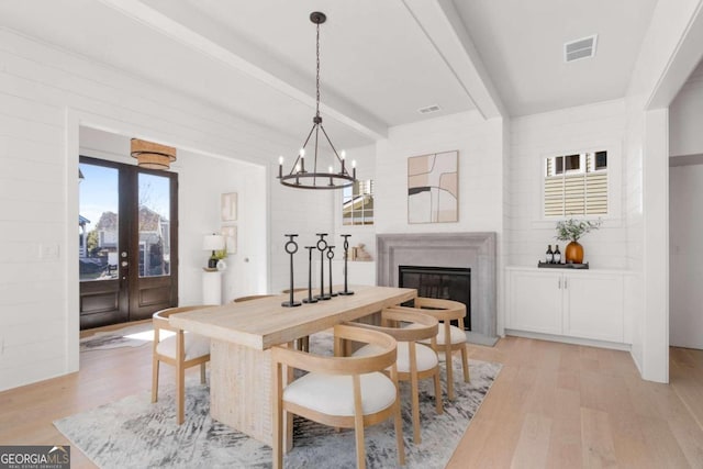 dining room with beam ceiling, an inviting chandelier, and light wood-type flooring