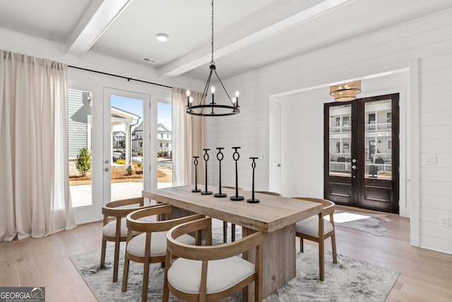 dining room featuring wood walls, visible vents, light wood-style floors, french doors, and beamed ceiling