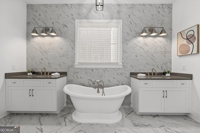 full bath featuring a soaking tub, marble finish floor, two vanities, and a sink