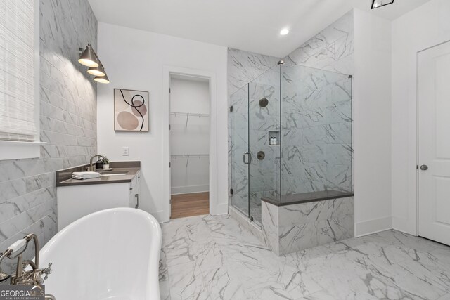 bathroom featuring a walk in closet, marble finish floor, a marble finish shower, a soaking tub, and vanity