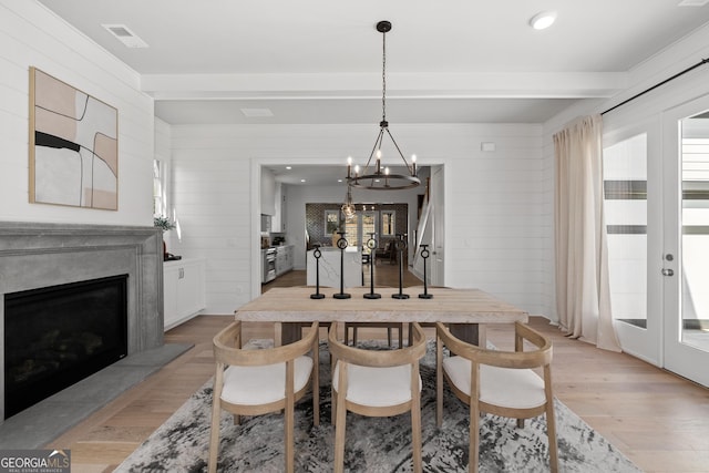 dining area with french doors, visible vents, light wood-style floors, a high end fireplace, and beamed ceiling