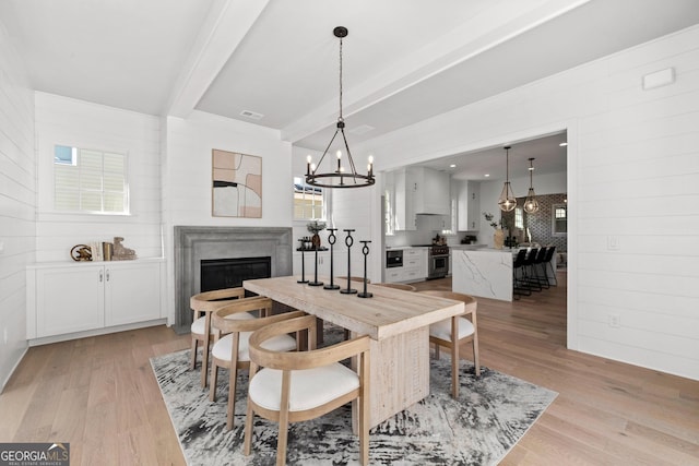 dining space with visible vents, a fireplace, beamed ceiling, and light wood-style flooring