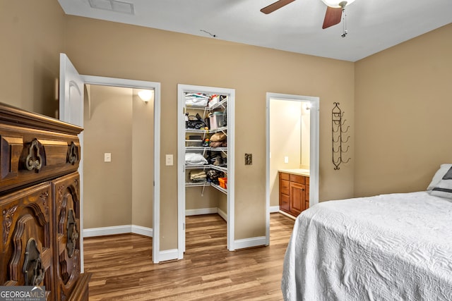 bedroom featuring ceiling fan, ensuite bath, light hardwood / wood-style flooring, and a walk in closet