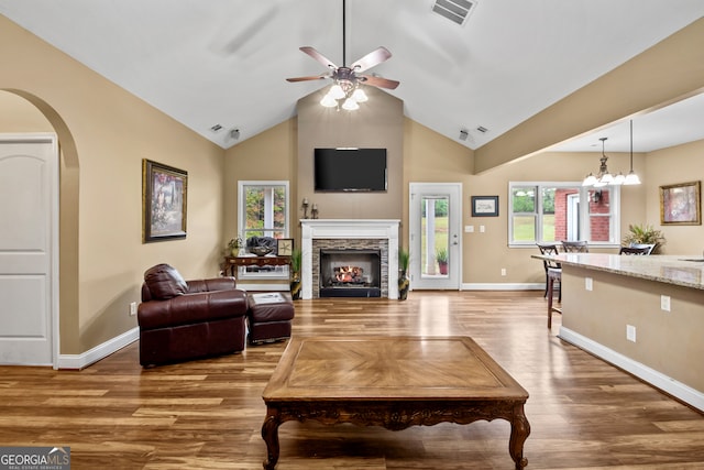 living room with a stone fireplace, ceiling fan with notable chandelier, hardwood / wood-style flooring, and high vaulted ceiling