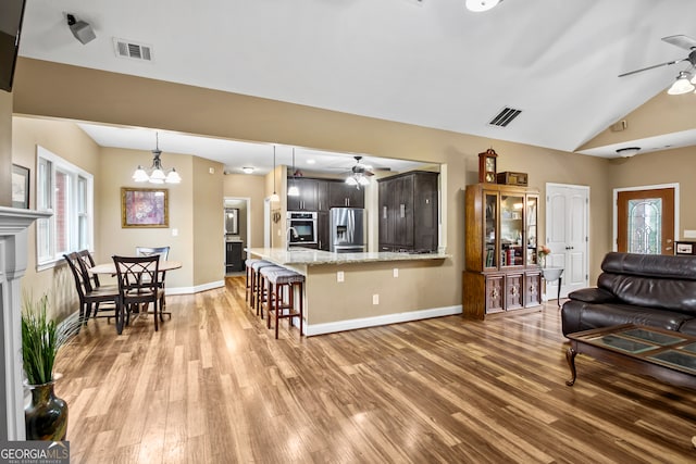 living room featuring light wood-type flooring, vaulted ceiling, and ceiling fan with notable chandelier