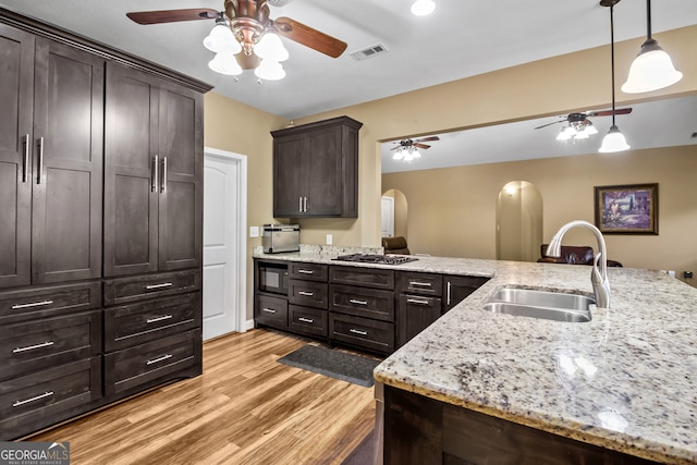 kitchen featuring sink, built in microwave, dark brown cabinets, light wood-type flooring, and decorative light fixtures