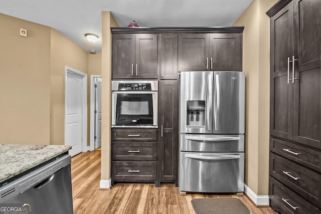 kitchen with stainless steel appliances, light stone countertops, dark brown cabinets, and light wood-type flooring