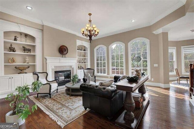 living room with dark wood-type flooring, a notable chandelier, ornamental molding, and built in shelves