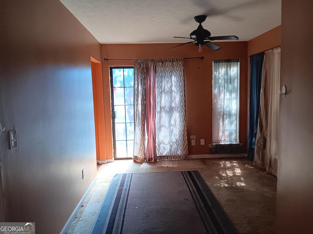 unfurnished room with ceiling fan, a textured ceiling, and light carpet