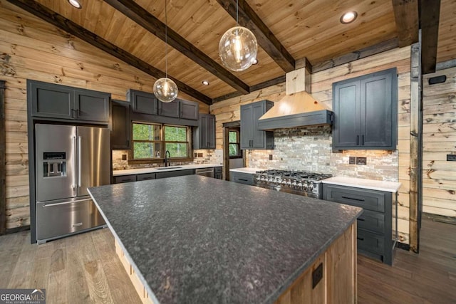 kitchen with wood walls, vaulted ceiling with beams, stainless steel appliances, pendant lighting, and custom exhaust hood