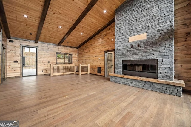 unfurnished living room featuring wooden walls, high vaulted ceiling, beamed ceiling, and light wood-type flooring