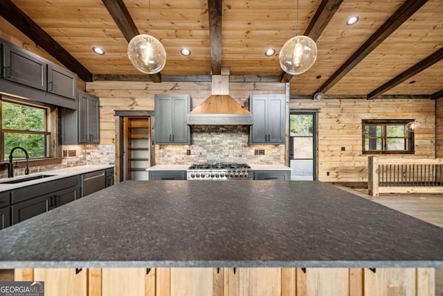 kitchen featuring sink, a spacious island, hanging light fixtures, wooden walls, and premium range hood