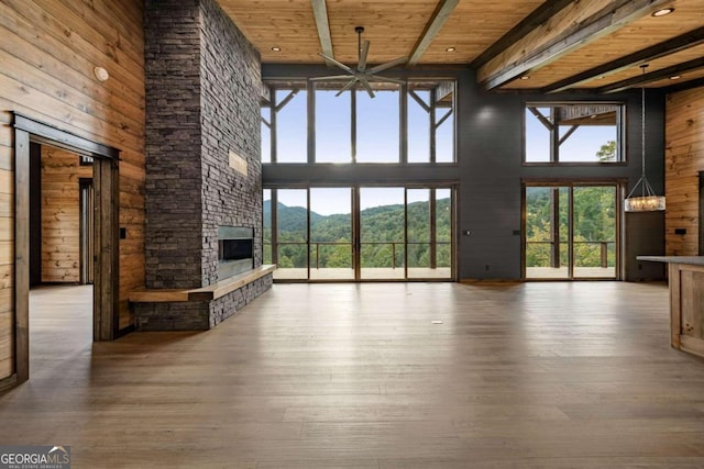 unfurnished living room featuring wood-type flooring, a stone fireplace, wooden ceiling, a high ceiling, and beamed ceiling