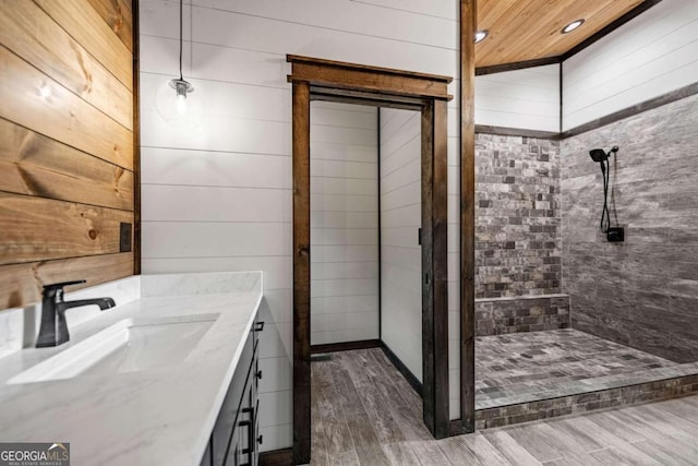 bathroom with vanity, wood walls, a tile shower, and wood-type flooring